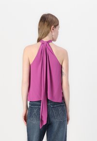 Fialová halter top z ľahkej tkaniny s drapériou na chrbte a viazaním, spojená s modrými džínsami, ktoré majú vyšívané vrecká.