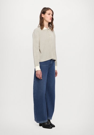 Camicia a maniche lunghe beige a righe chiare con colletto bianco, abbinata a pantaloni in denim blu larghi. Stivaletti neri alla caviglia completano l'outfit.