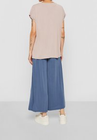 Ljusbeige kortärmad topp kombinerad med blå vida byxor, båda gjorda av mjuk tyg. Outfiten har en avslappnad passform och enkel design.