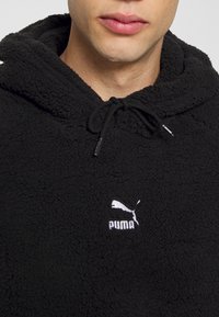 Black fleece hoodie with a textured finish. Features a drawstring hood and a white embroidered Puma logo on the chest.