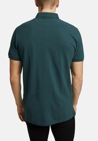 Donkergroene polo met een kraag en korte mouwen. Gladde textuur, aansluitend ontwerp en subtiele stikdetail aan de achterkant.