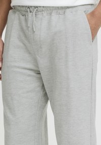 Pantalon de survêtement gris en tissu doux, doté d'une taille élastique avec cordon de serrage, de poches latérales et d'une coupe décontractée.