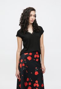 Svart topp med korte ermer og blonder i V-hals, kombinert med svart skjørt med store røde blomster. Jevn stofftekstur.