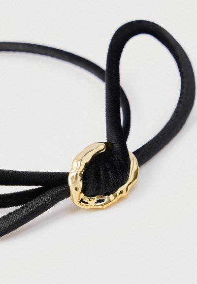 Șnur din țesătură neagră cu o cataramă texturată din aur, având o secțiune noduroasă pentru lungime reglabilă.