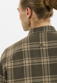 Donkergroene geruite shirt gemaakt van een zachte stof, met een button-down kraag, opvallende beige strepen en een klein logo op de achterkant.