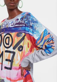 Kleurrijke longsleeve trui met een levendig multicolor grafisch ontwerp, voorzien van grijze mouwen en grote zwarte tekst aan de voorkant.