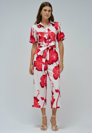 Tuta floreale con base bianca e grandi fiori rossi, maniche corte, colletto e vita legata. Tessuto testurizzato con vestibilità comoda.