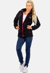 Schwarze Fleecejacke mit rosa Reißverschluss und Akzenten, ausgestattet mit einem hohen Kragen und zwei Vordertaschen, kombiniert mit blauen Jeans und weißen Sneakers.
