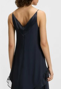 Granatowa sukienka bez rękawów z dekoltem w kształcie litery V, z zapięciem na zamek błyskawiczny i delikatnym, opadającym dołem z przezroczystymi akcentami.