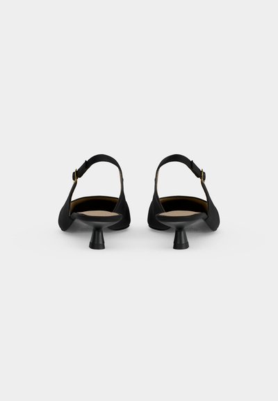 Paire d’escarpins slingback noirs à talons bas évasés et brides à la cheville, vus de dos sur un fond clair et uni.