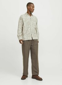 Cămașă lejeră, cu mânecă lungă, în nuanță deschisă de bej, cu un model paisley, asortată cu pantaloni maro cu talie înaltă și pantofi maro închis.