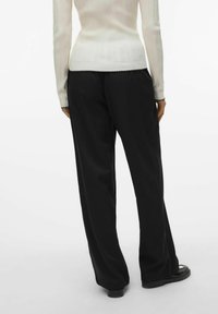 Pantalon noir à jambes larges avec une texture lisse, associé à un top blanc à manches longues avec une finition à bords festonnés.