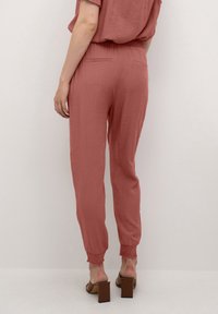 Roze, gestructureerde broek met een elastische tailleband en geribbelde manchetten. Voorzien van twee achterzakken. Gecombineerd met bruine sandalen met blokhak.
