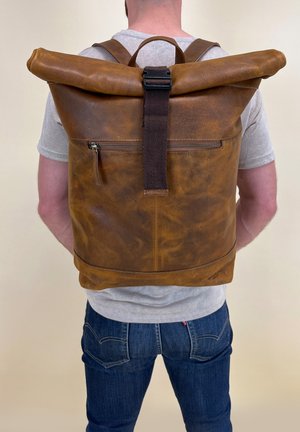Brown leather roll-top backpack featuring a front zipper pocket, adjustable straps, and a textured finish. Back view shown.