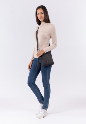 Borsa a tracolla nera con superficie texturizzata e dettaglio a frange; indossata da un modello in una maglia beige e jeans blu, con sneakers bianche.
