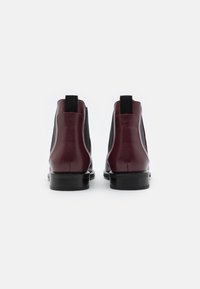Botas de tobillo de cuero burdeos con paneles laterales elásticos y acentos negros. Textura suave con un tacón bajo de goma negra. Diseño simple.