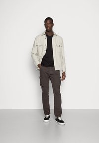 O jachetă ușoară gri deschis peste un tricou negru, combinată cu pantaloni cargo gri închisi și adidași negri cu tălpi albe. Croială dreaptă și design minimalist.