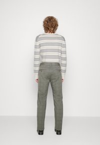 Suéter a rayas en gris y blanco hueso, combinado con pantalones texturizados verdes; cuenta con un corte recto y bolsillos traseros. Zapatos negros completan el conjunto.