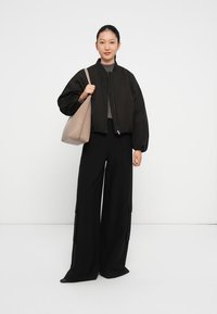 Zwarte gewatteerde bomberjack, grijze top, zwarte wijde broek met zakken, houdt een beige tote bag vast. Eenvoudig ontwerp, gladde textuur, neutrale kleuren.