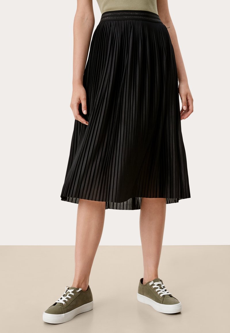 Svart plisserad midikjol med en texturerad yta och elastisk midja, kombinerad med gröna sneakers med vita snören och en kraftig sula.