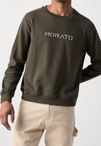 Mörkgrön sweatshirt med ribbade ärmslut och nederkant, med ordet "MORATO" tryckt i en kontrasterande färg över bröstet.