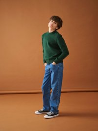 Grön stickad tröja, blå löst sittande jeans och svarta låga sneakers. Enklare design med rundad halsringning och strukturerad stickad textil.