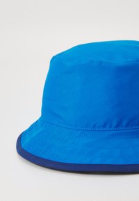 Blå bucket-hatt i slätt tyg, med en bred, nedåtlutande brätte och en kontrasterande marinblå kant vid basen.
