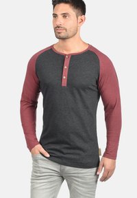 Langärmliges Henley-Shirt mit grauem Körper und burgunderfarbenen Ärmeln, ausgestattet mit drei Holzknöpfen am Kragen und einem dezenten Markenetikett.