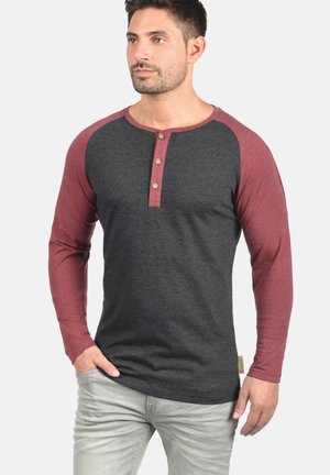 Camisa henley de manga larga con cuerpo gris y mangas burdeos, que presenta tres botones de madera en el escote y una etiqueta de marca sutil.