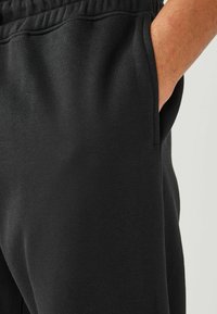 Pantalones de chándal negros hechos de una tela suave, con cinturilla elástica y bolsillos laterales, con una textura lisa y un diseño de pierna ajustada.