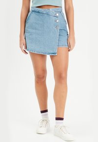 Jupe portefeuille en denim bleu clair avec un ourlet effiloché, dotée de trois boutons-pression en argent à l'avant et d'un design taille haute.