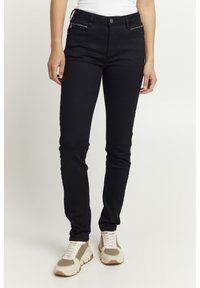 Melnas slim fit džinsi, kas izgatavoti no elastīga auduma. Iespējas ar rāvējslēdzēju sānu kabatām un pieguļošu dizainu, saskaņoti ar gaišas krāsas sporta apaviem.