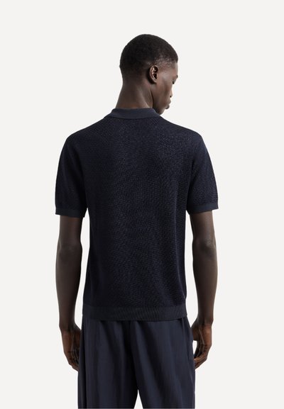 Polo shirt navy a maniche corte con un design a maglia testurizzata, colletto e polsini a coste e un leggero orlo finito.