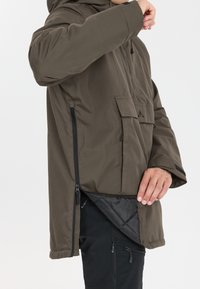 Ruskea hupullinen takki, jossa on vetoketjulla varustettu sivutuuletin ja etutasku. Ominaisuuksiin kuuluu kevyt, sileä tekstuuri ja rento istuvuus.