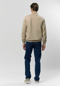 Béžová mikina s vysokým golierom, priliehavými manžetami a detailným švom na chrbte. Skombinovaná s tmavomodrými džínsy a svetlými teniskami.