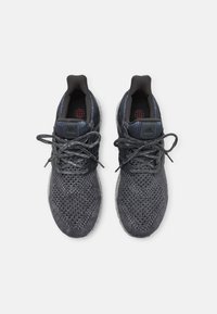 Black athletic shoes with a textured mesh upper, round laces, and a cushioned sole. Features a red logo on the insole and a streamlined design.