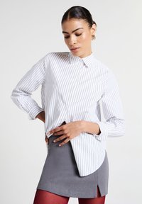 Camicia bianca con sottili righe nere, maniche lunghe e orlo curvo, abbinata a una minigonna grigia e collant rossi.