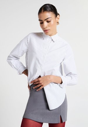 Camicia bianca con sottili righe nere, maniche lunghe e orlo curvo, abbinata a una minigonna grigia e collant rossi.