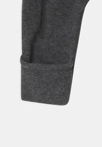 Grauer Fleece-Hosensaum mit glatter Textur, seitlicher Reißverschlussdetails. Der Stoff wirkt weich und dick.