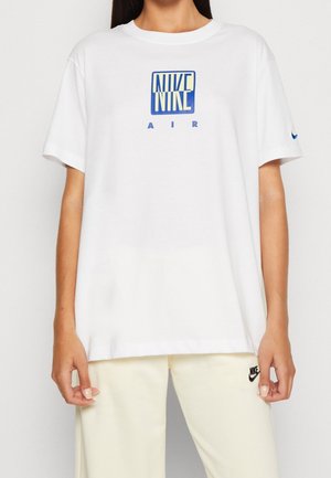 Camiseta blanca de algodón con un logo azul de Nike Air en la parte frontal. Cuello redondo y corte holgado con mangas cortas.