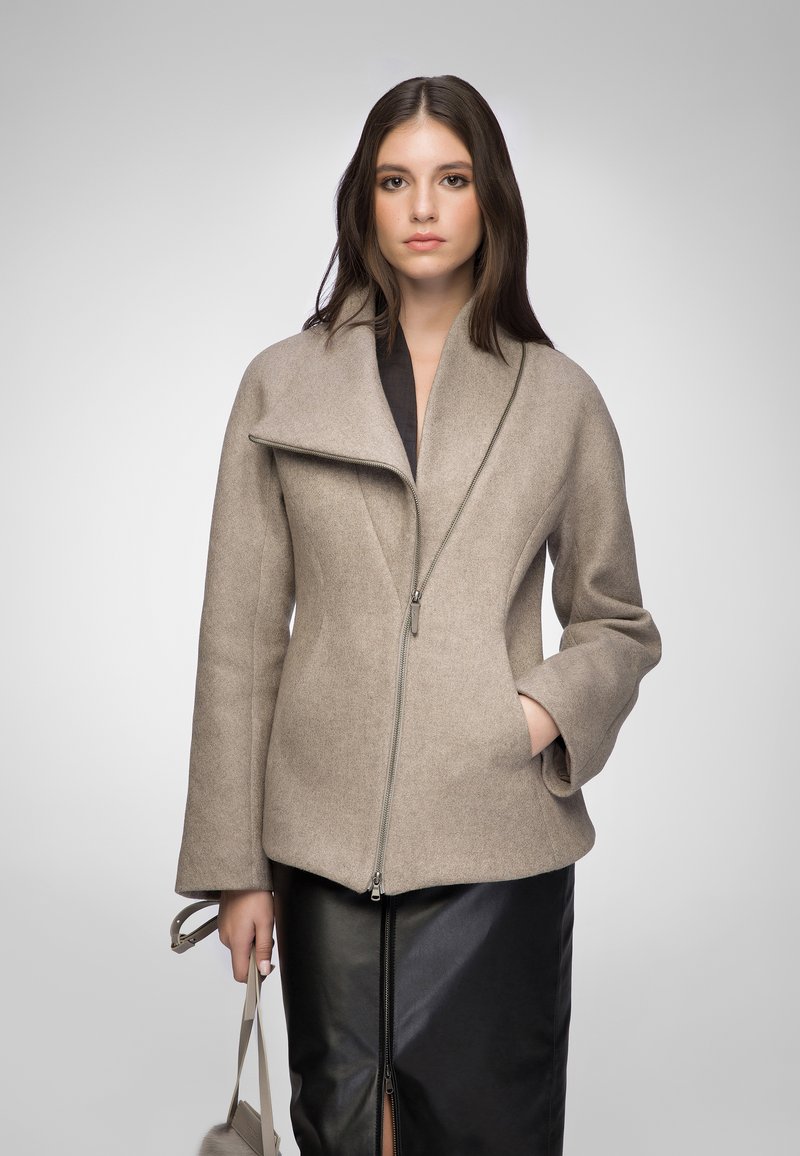 Beige wool-blend jacket with a high collar, asymmetric zip front, and two side pockets, paired with a black leather skirt.