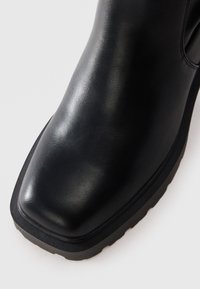 Black leather ankle boot with a rounded toe, smooth texture, and a durable rubber sole. Features minimal stitching and a slip-on design.