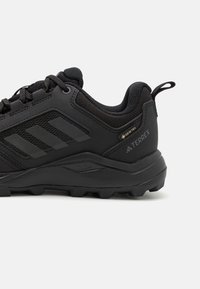 Black hiking shoe with textured mesh and synthetic upper, featuring three stripes design, cushioned heel, and rugged outsole for traction.
