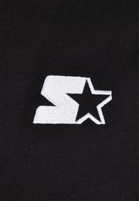 Zwarte stof met een witte geborduurde logo, met een gestileerde letter "S" en een ster, die een gladde textuur en een strak ontwerp laat zien.