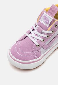 Baskets montantes en suède violet avec lacets blancs, semelle en caoutchouc et intérieur jaune, présentant des accents de couture et une étiquette de logo sur la languette.