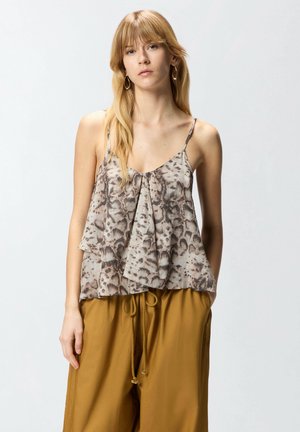 Donna bionda che indossa orecchini a cerchio, un top senza maniche con stampa animalier e balza frontale, e pantaloni giallo senape con coulisse.