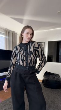 Svart och cremefärgad randig kofta med knäppning och ribbad nederkant, kombinerad med svarta högmidjade byxor och placerad mot en neutral bakgrund.