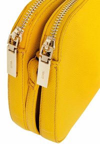 Żółta skórzana torba crossbody z podwójnymi metalowymi zamkami błyskawicznymi, teksturowaną powierzchnią i widocznymi detalami szwalniczymi. Posiada srebrne akcenty metalowe.