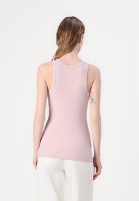 Light pink fitted tank top with a rounded neckline and wide straps. Ribbed texture, smooth fabric, and a hip-length cut.