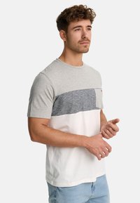 Lys grå bomulds t-shirt med et vandret blokdesign, der har en marineblå stribe, en hvid nederste sektion og en brystlomme.